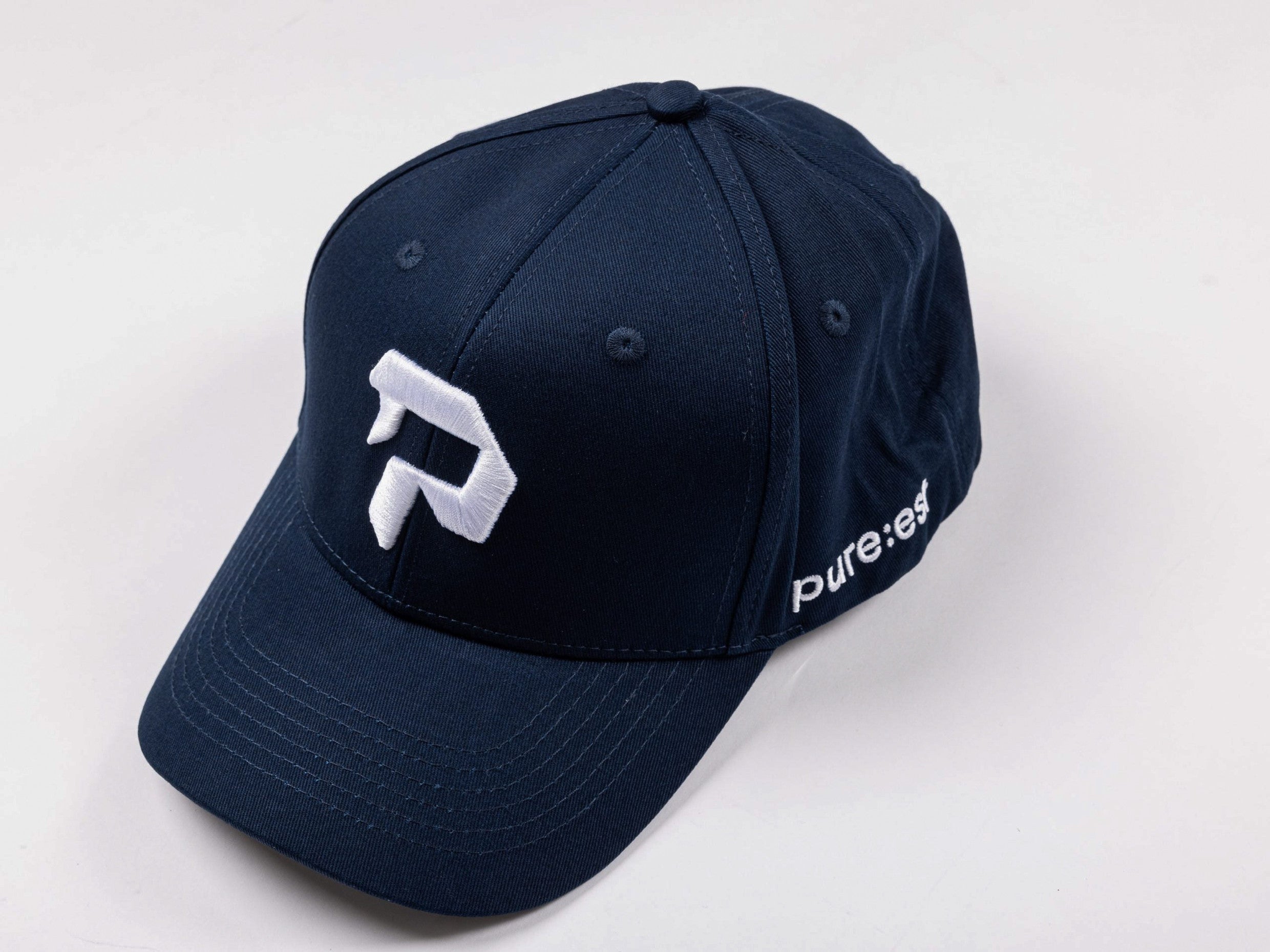 pureest keps. Broderad logo i vitt & mörkblå tyg